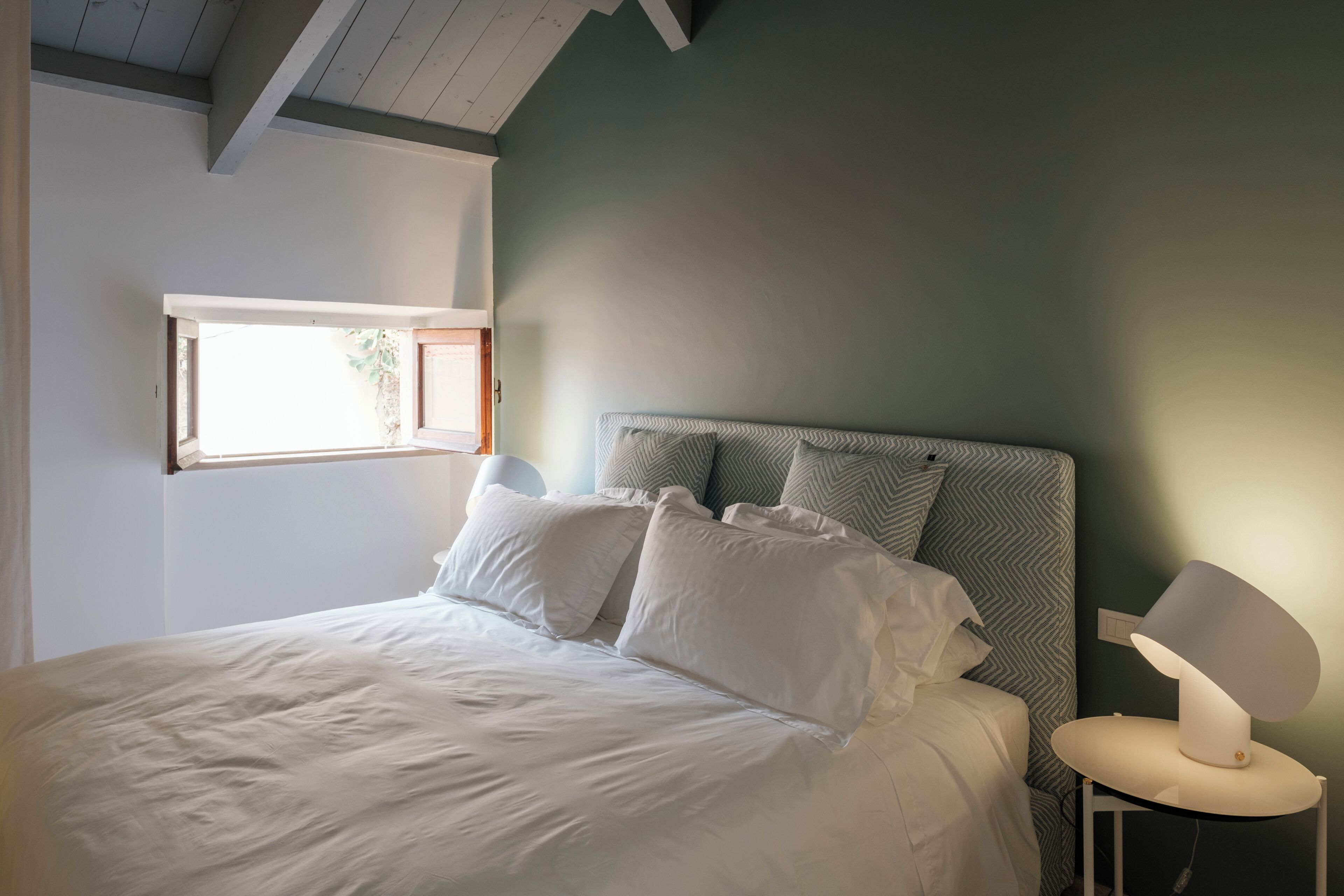 A bedroom with a bed, pillows, a bedside lamp, and a window.