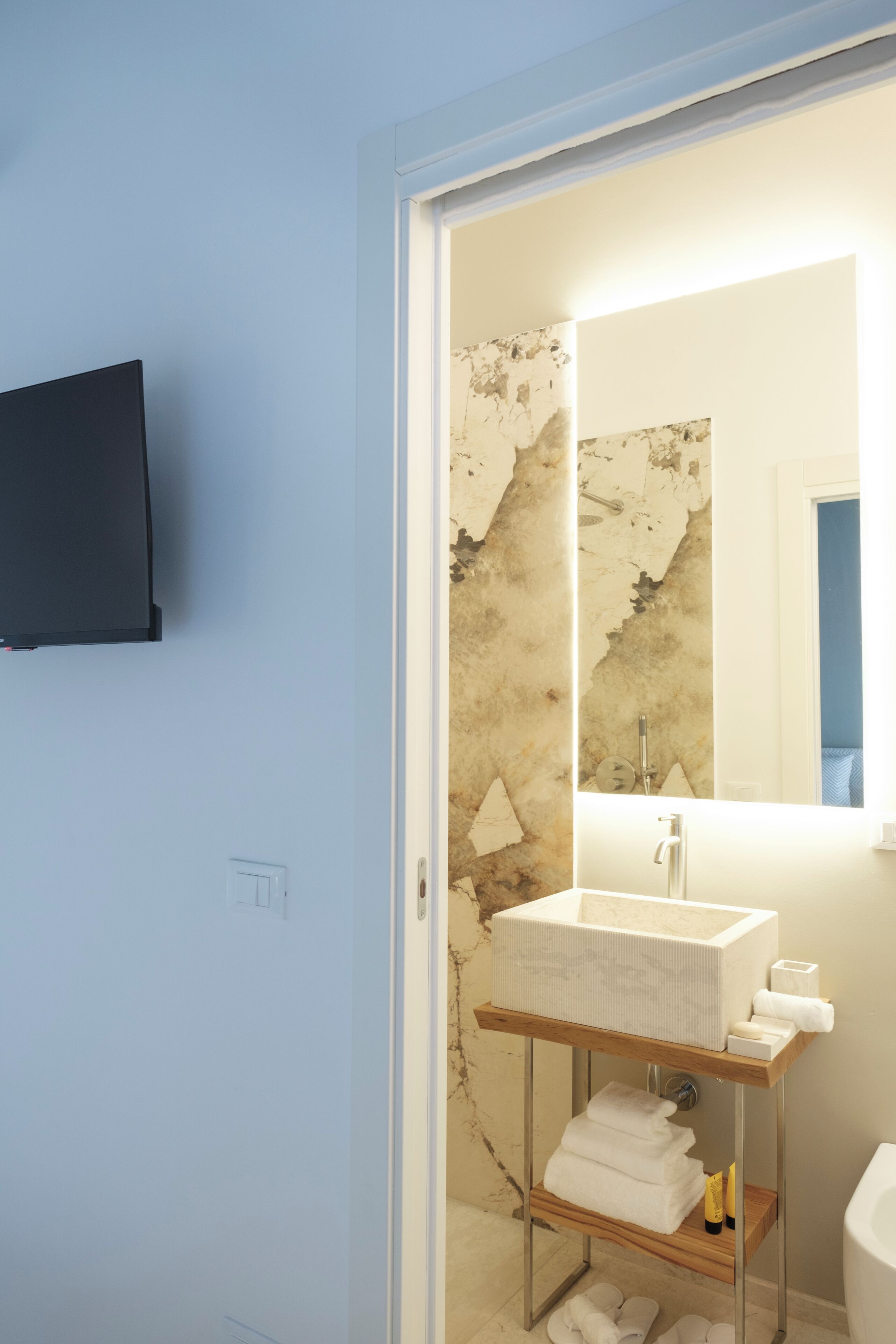 Ein Badezimmer mit Waschbecken, Spiegel und einem an der Wand montierten Fernseher.