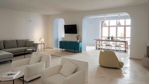 A modern living room with a sofa, armchairs, a teal sideboard, a flat-screen TV, and a dining area with a table and chairs. - La Balza di Scilla (Scilla)