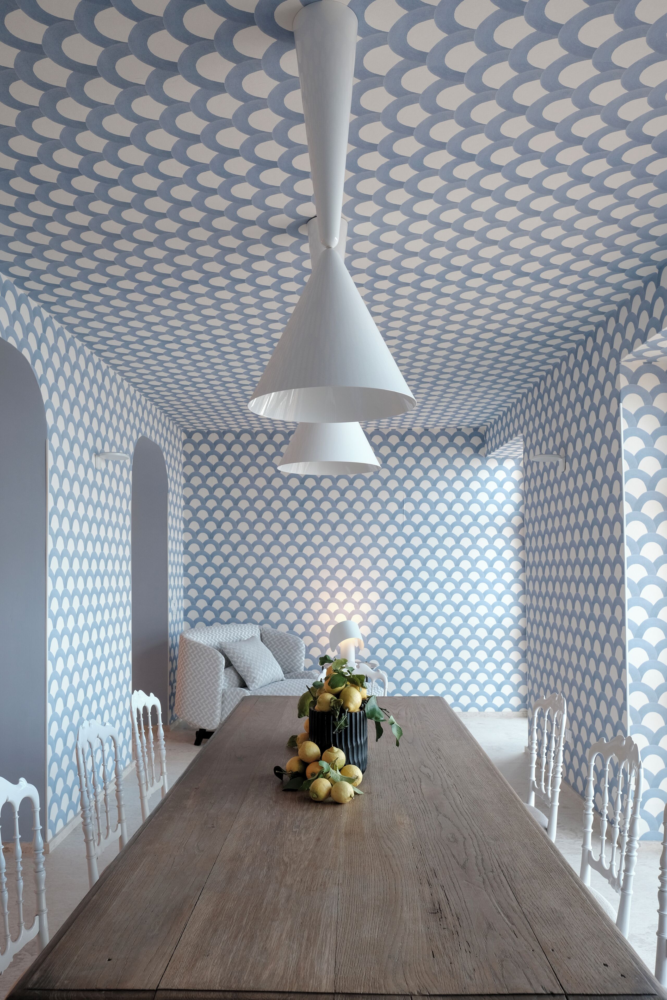 A dining area with a wooden table, white chairs, a patterned ceiling, and a hanging light fixture.