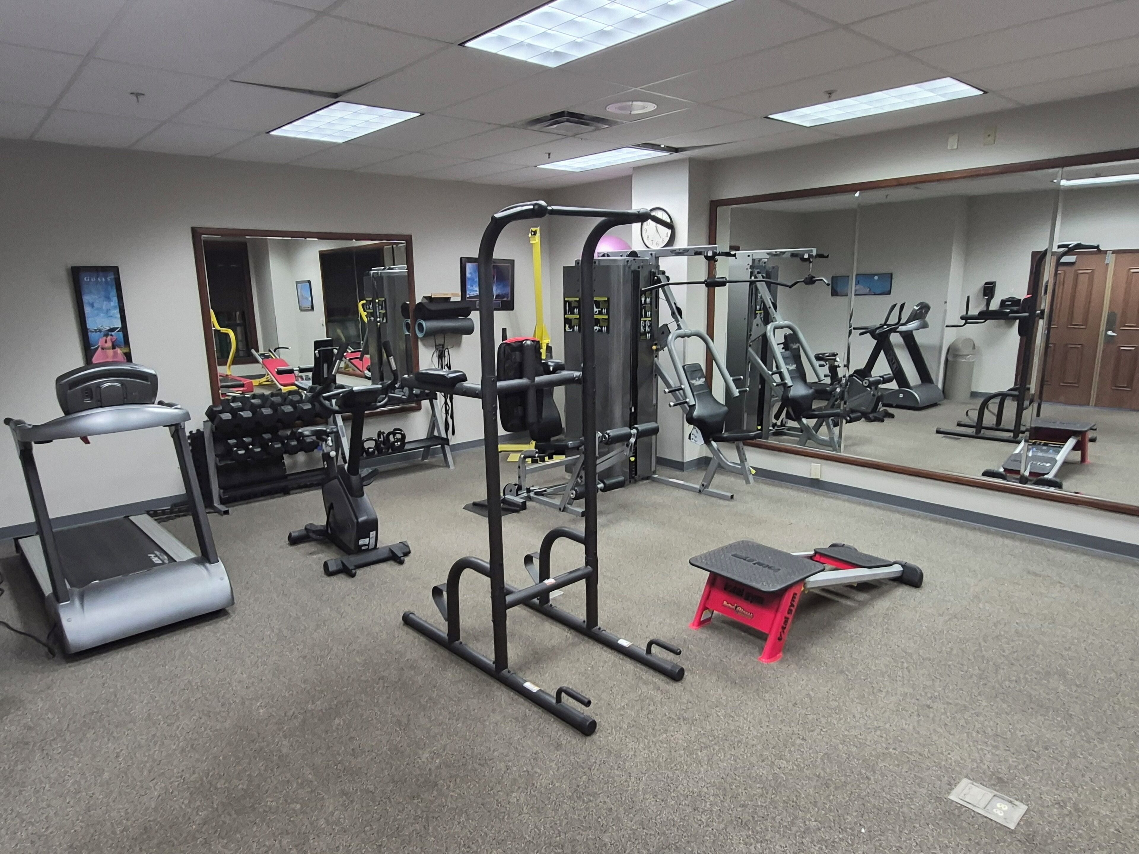 Une salle de sport équipée de divers appareils d’exercice, notamment des tapis de course, des appareils de musculation et des poids libres.