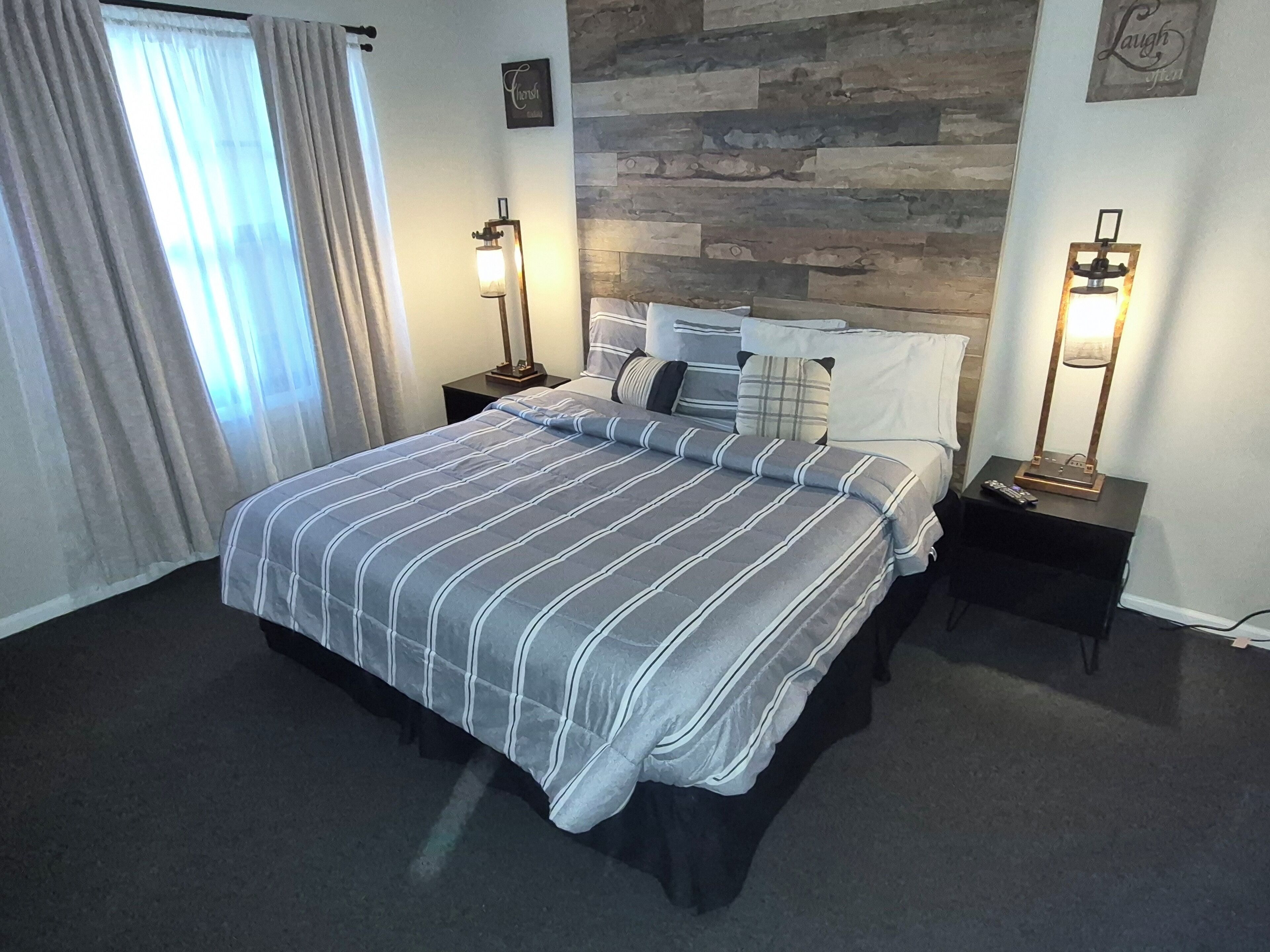 Habitación de hotel con cama, dos mesitas de noche, una lámpara de pared y una ventana con cortinas, además de una pared con textura de piedra.