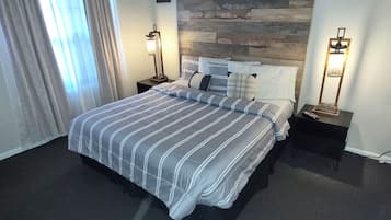 Habitación de hotel con cama, dos mesitas de noche, una lámpara de pared y una ventana con cortinas, además de una pared con textura de piedra.