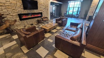 Un hall con paredes de piedra, muebles de cuero, chimenea y televisor.