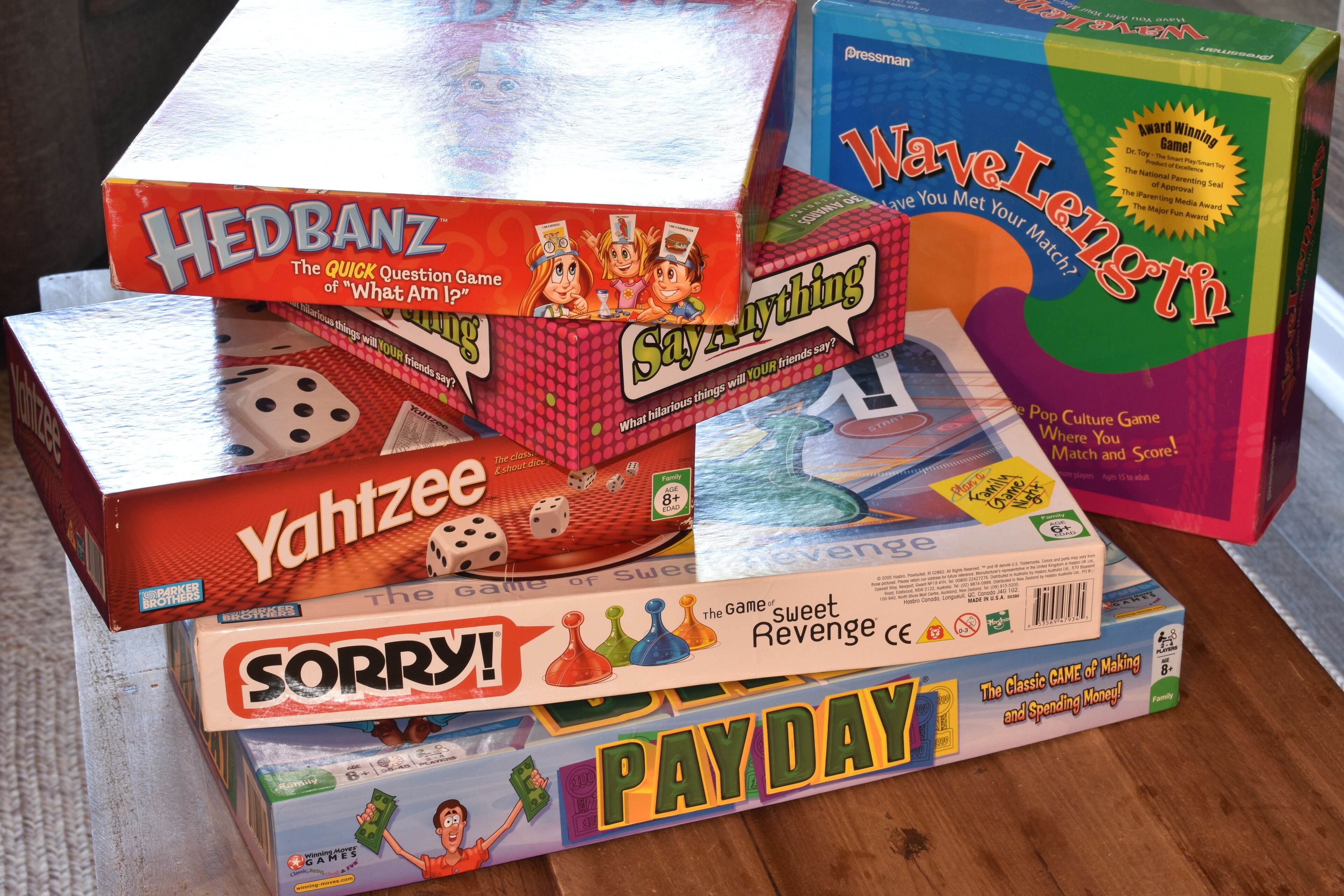 A collection of board games including Hedbanz, Yahtzee, Sorry!, and others, arranged on a wooden surface.