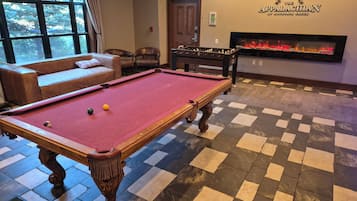 Una mesa de billar con bolas, un sofá, una mesa de fútbol de mesa y una chimenea.
