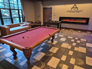 Een pooltafel met ballen, een bank, een tafelvoetbalspel en een open haard.