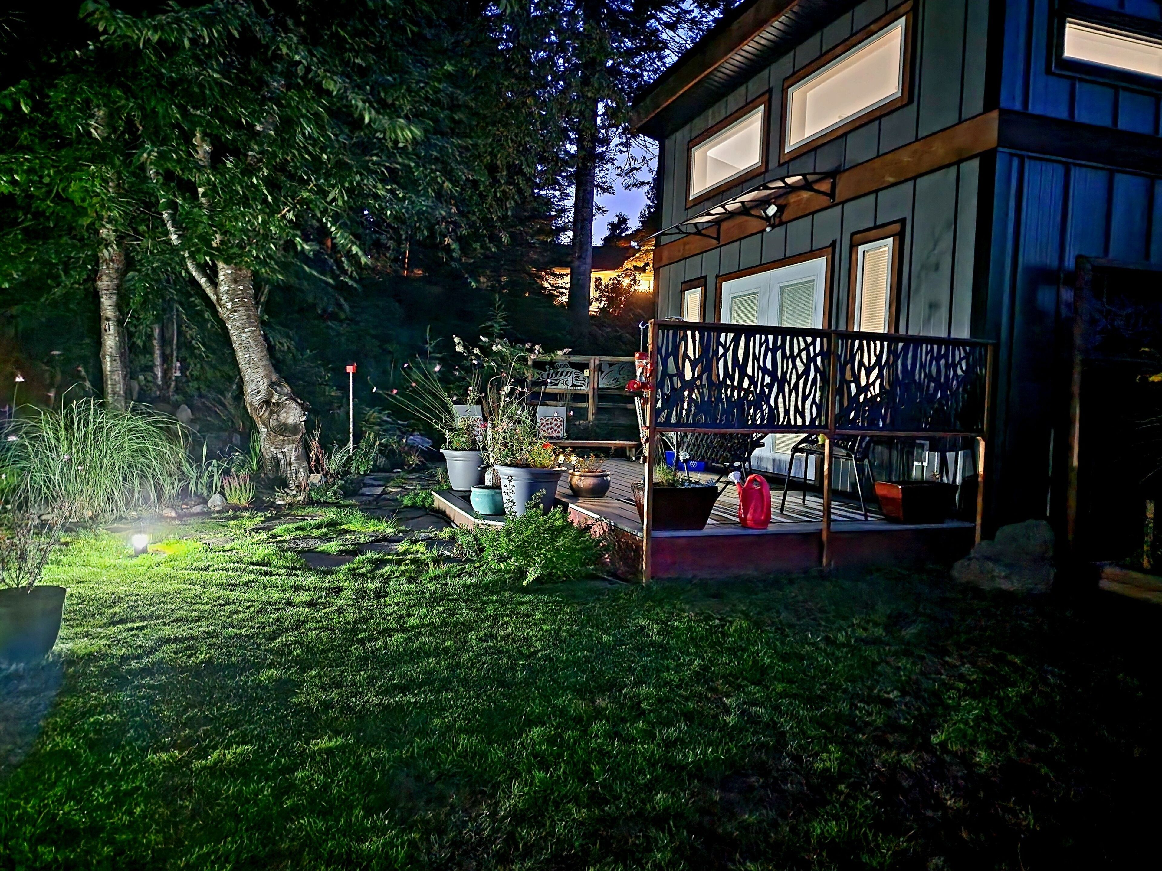 A modern house with a deck, potted plants, and a well-maintained lawn.