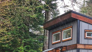 Une maison à deux étages dotée d’un balcon, d’une terrasse couverte et d’un jardin agrémenté de plantes en pot.