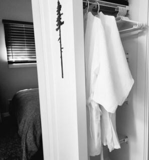 Een slaapkamer met een bed, een raam met zonwering en een kast met hangende kleding.