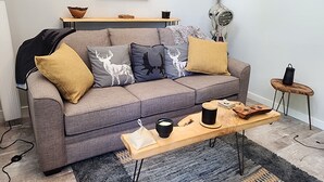 Un salon moderne avec un canapé gris, des coussins décoratifs, une table basse en bois et un tableau accroché au mur.