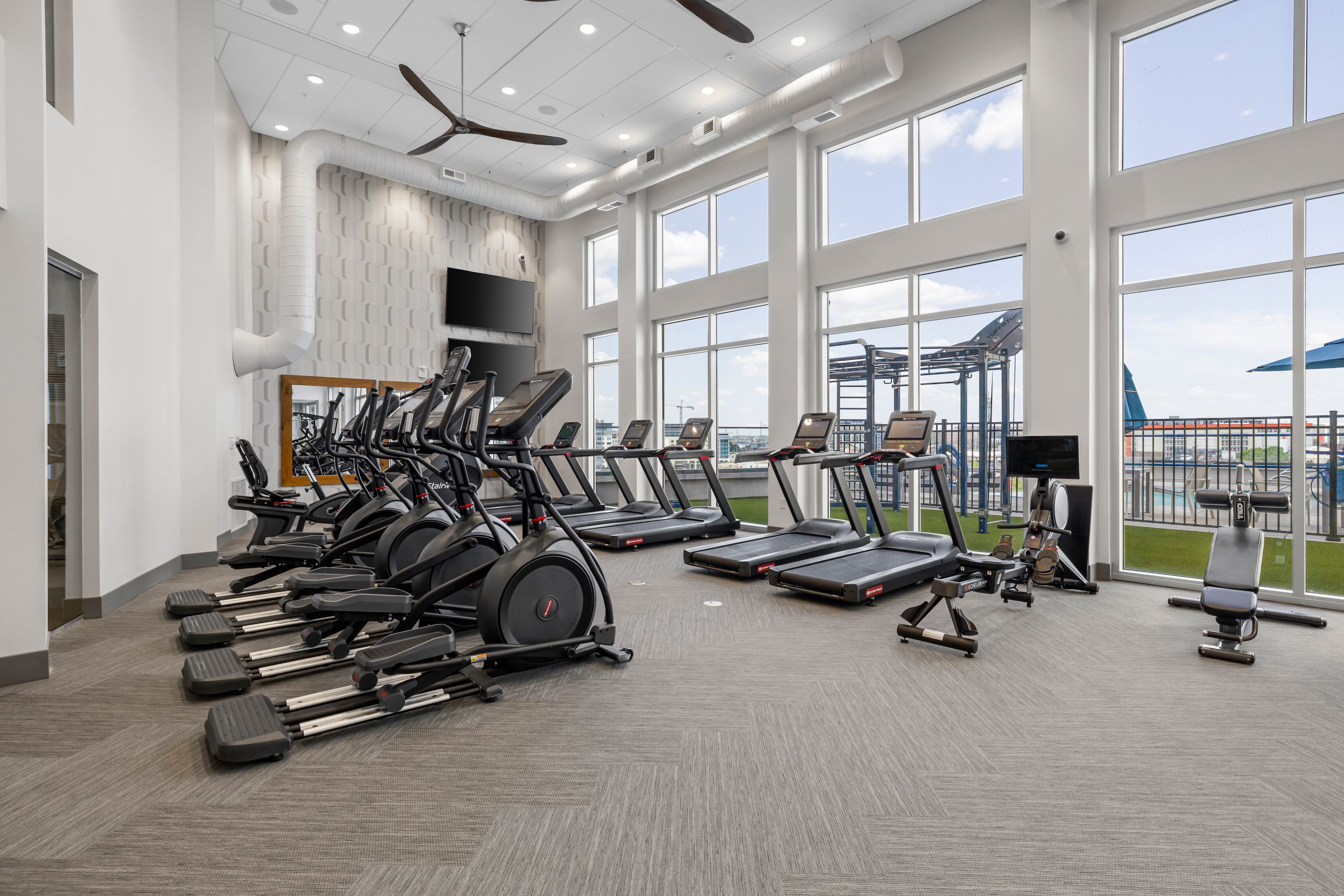 Un gimnasio moderno con cintas de correr, elípticas y una máquina de remo.