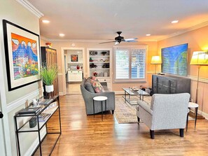 A living room with a sofa, armchair, and TV, wooden flooring, and a ceiling fan. - Pleasant Downtown Haven *0.3 Miles *Pet Friendly (Prescott)