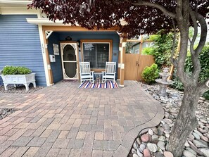 A patio with a brick floor, two white chairs, a small table, and a decorative fountain. - Pleasant Downtown Haven *0.3 Miles *Pet Friendly (Prescott)