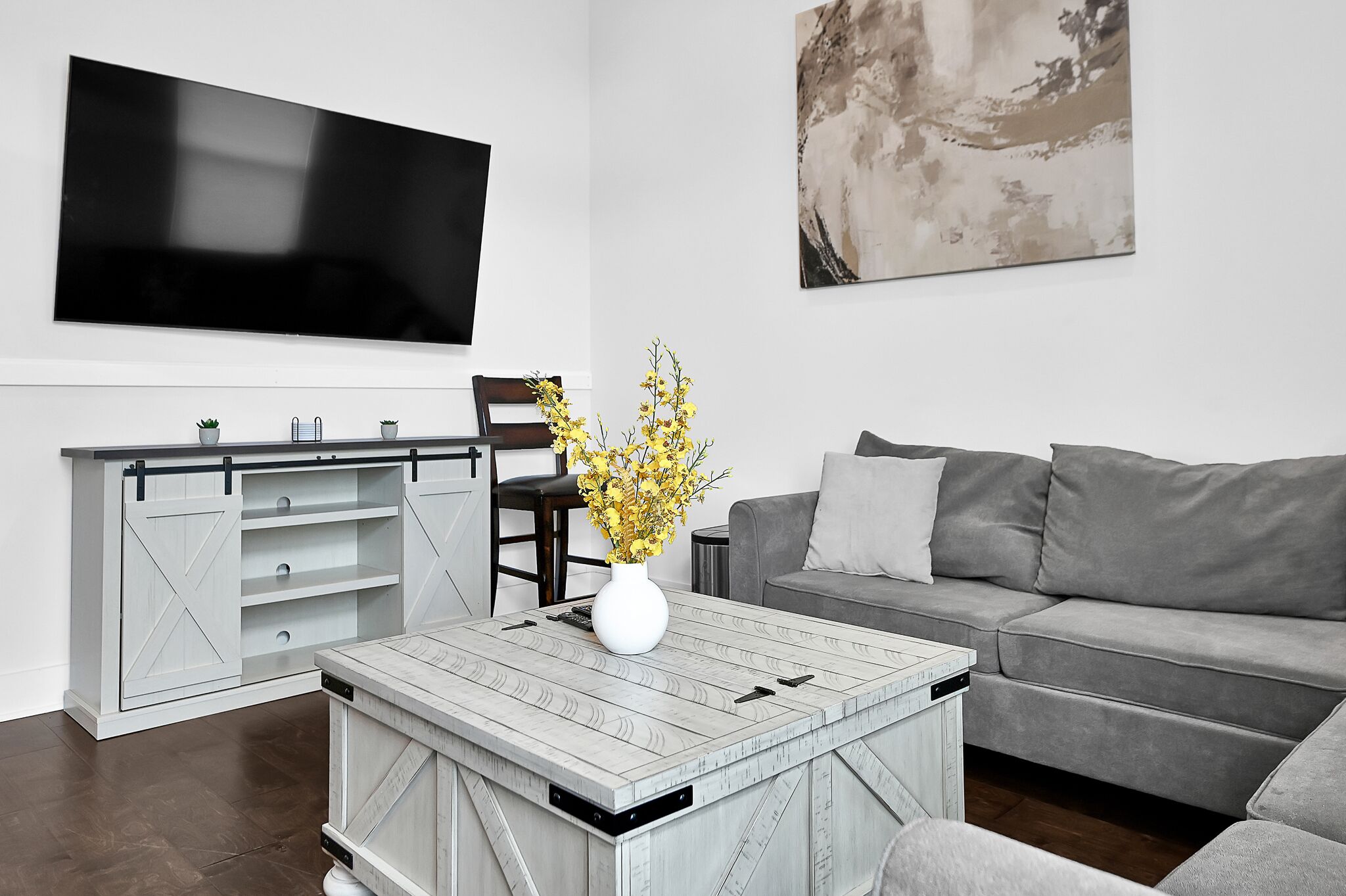 Un salon moderne doté d’un téléviseur à écran plat, d’un canapé gris, d’une table basse surmontée d’un vase blanc et d’un meuble à portes coulissantes de style rustique.