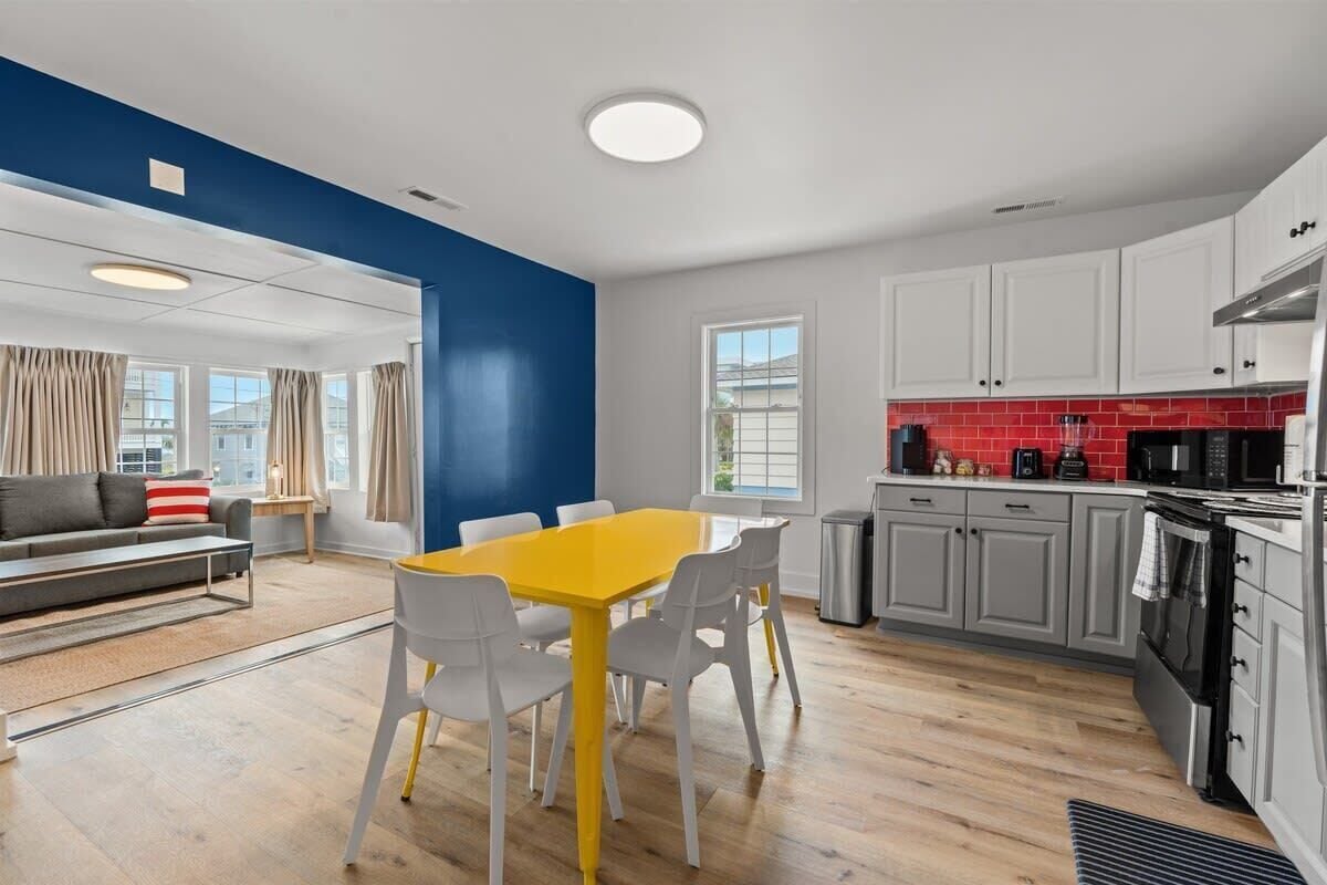 A modern kitchen with white cabinets, a red backsplash, and a dining area with a yellow table and white chairs.