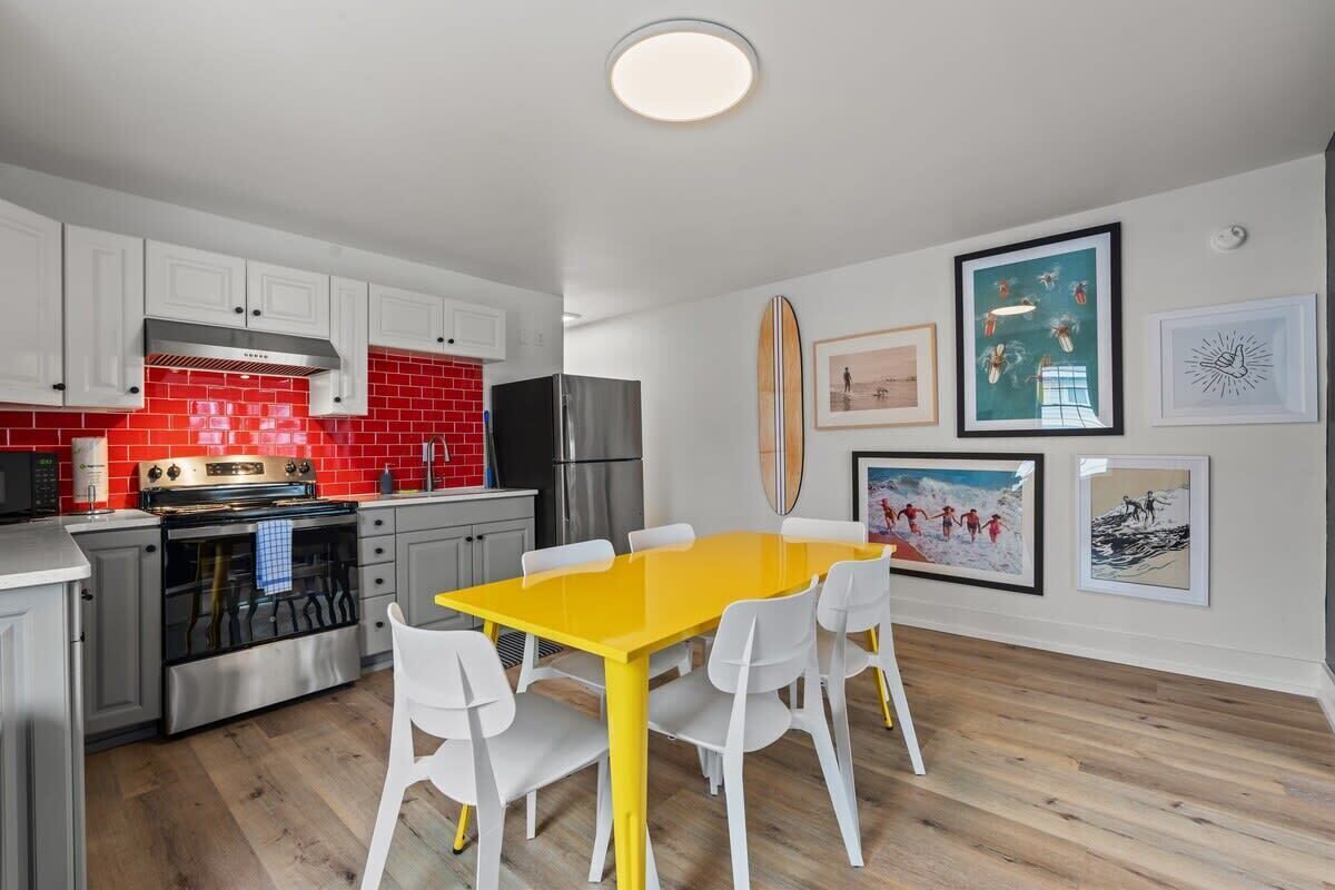 A modern kitchen with white cabinets, a red backsplash, and a yellow dining table with white chairs.