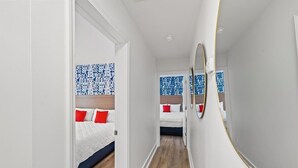 Un pasillo estrecho que conduce a un dormitorio con cama, espejo y papel tapiz estampado.