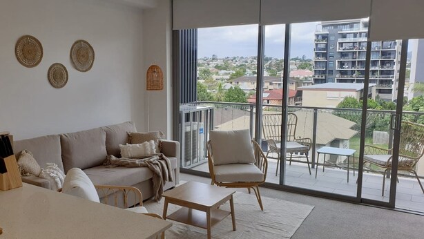 A modern living room with a sofa, a dining table, and a balcony with outdoor furniture. - Peaceful One Bedroom Residence with Parking (Brisbane)