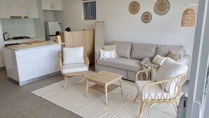 A modern living room with a sofa, two wicker chairs, a coffee table, and a kitchen area with white cabinets and a gas stove. - Peaceful One Bedroom Residence with Parking (Brisbane)