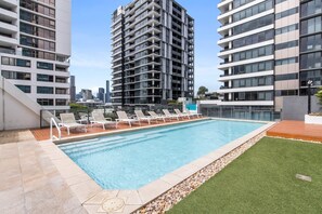 A modern building with a rooftop pool, lounge chairs, and a city skyline in the background.