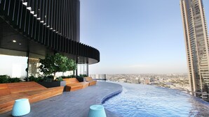 A rooftop infinity pool with a curved edge, wooden seating areas, and a view of the cityscape. - Two Bedroom Two Bathroom | First Class Residence on Queen St, Brisbane CBD (Brisbane)