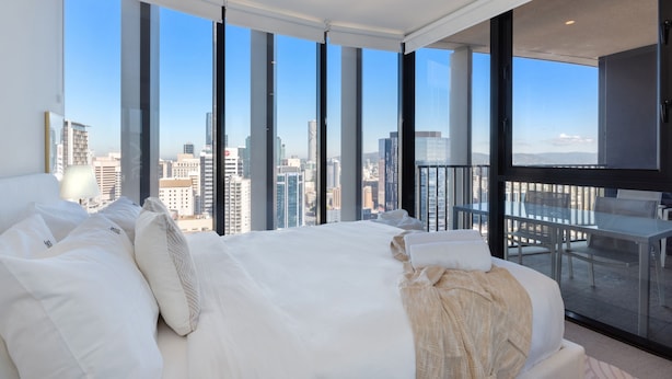 A modern hotel room with a large bed, a balcony with a glass table, and a city view. - Two Bedroom Two Bathroom | First Class Residence on Queen St, Brisbane CBD (Brisbane)