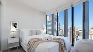 A modern hotel room with a large bed, a bedside table, a lamp, and a view of the cityscape through floor-to-ceiling windows. - Two Bedroom Two Bathroom | First Class Residence on Queen St, Brisbane CBD (Brisbane)