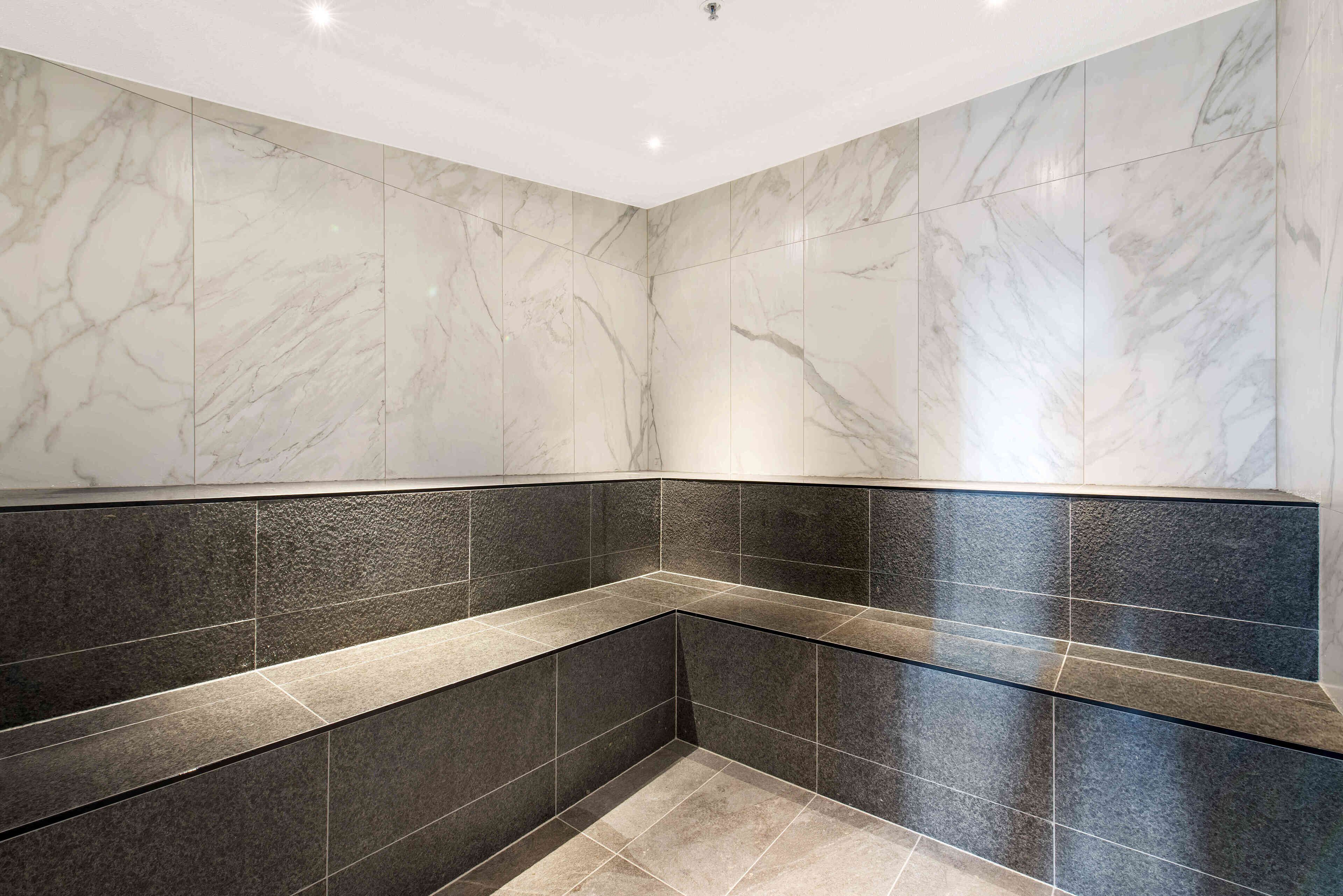 A bathroom with marble walls and dark tiles.