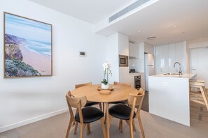 A modern kitchen with white cabinets, a central island with a sink, and a dining area with a wooden table and chairs.