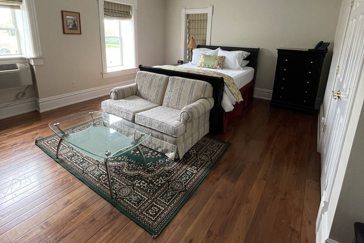 A spacious room with hardwood floors, a large bed with a headboard, a sofa, and a glass coffee table.