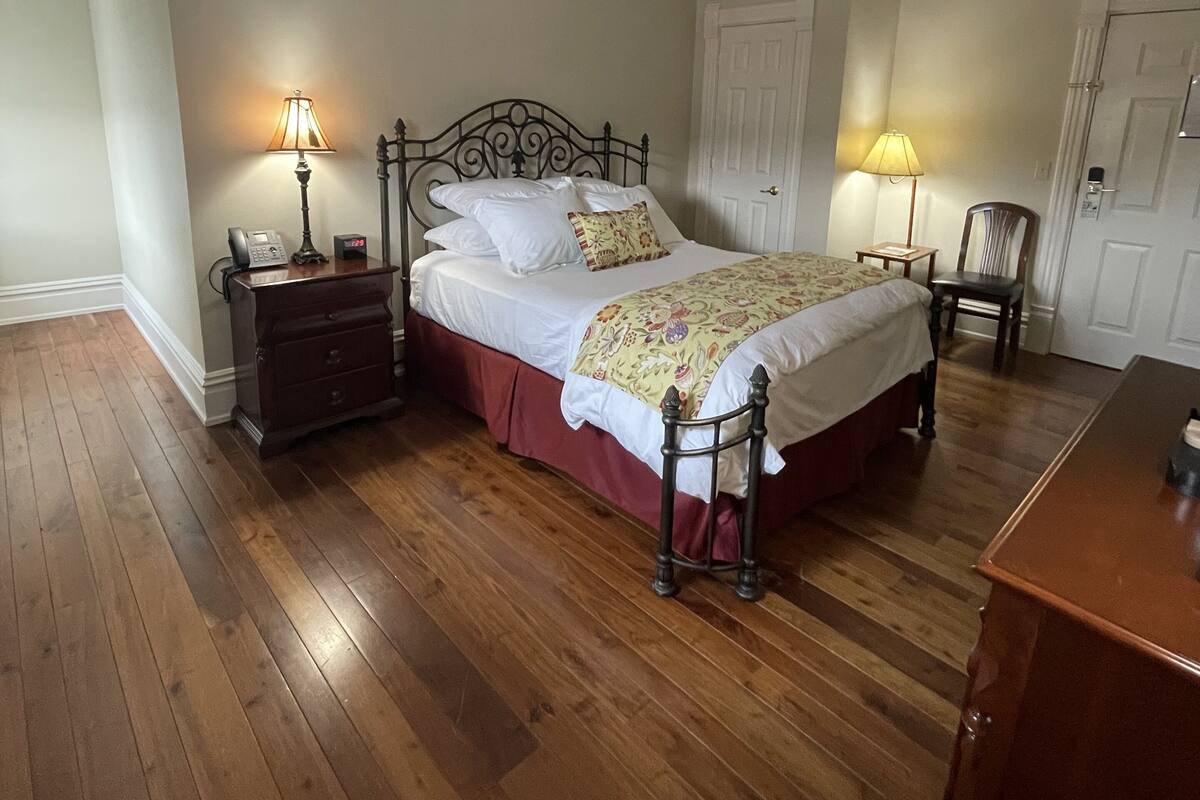 A bedroom with a wooden floor, a bed with white linens, two bedside tables with lamps, and a wooden dresser.
