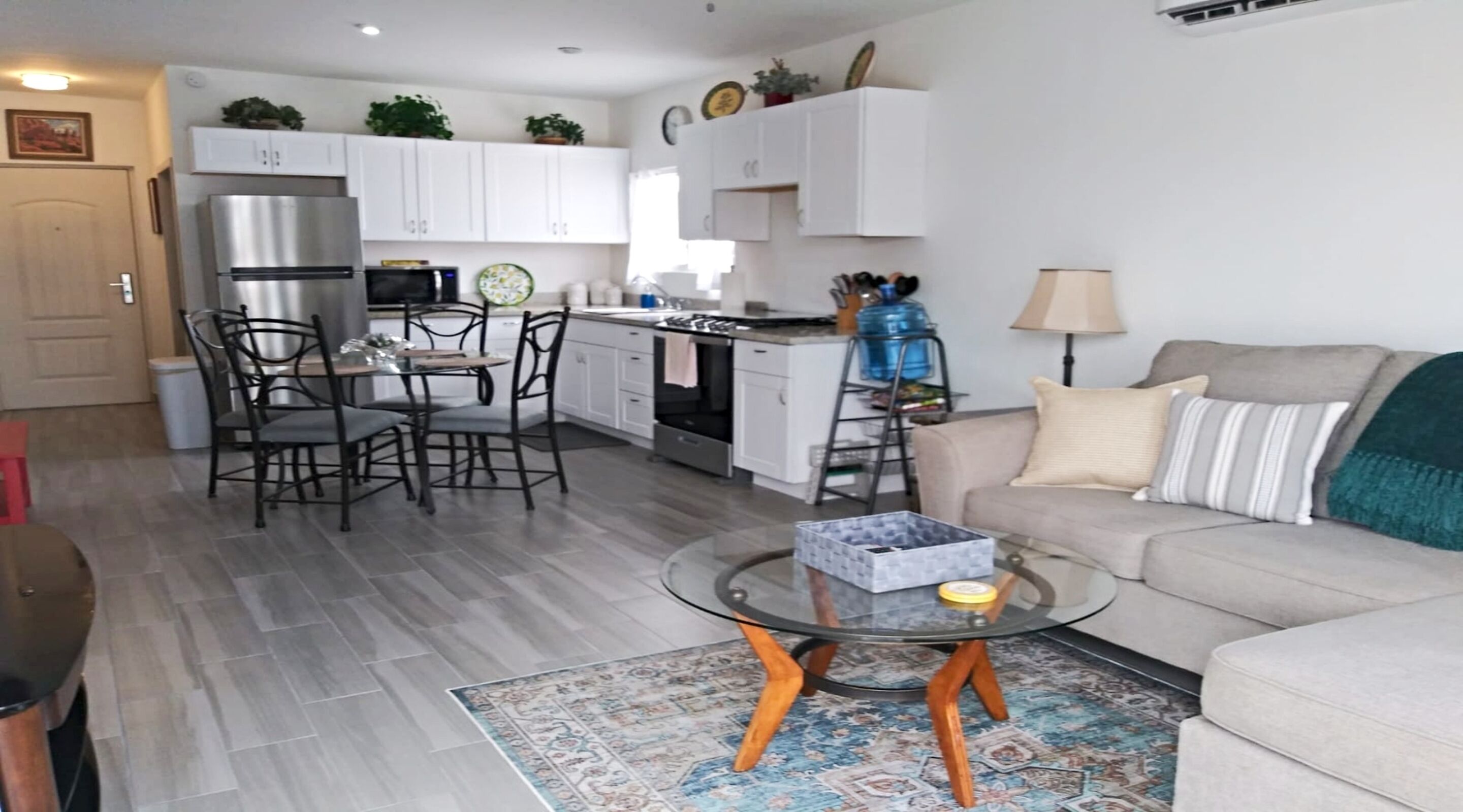 A modern kitchen with white cabinets, a stainless steel refrigerator, and a dining area with a glass table and chairs.