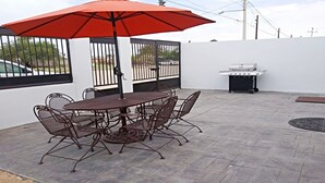 An outdoor patio with a round metal table and chairs, a red umbrella, and a barbecue grill.