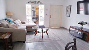 A living room with a sofa, a glass coffee table, a rug, a side table, a chair, and a console table with a vase of flowers.