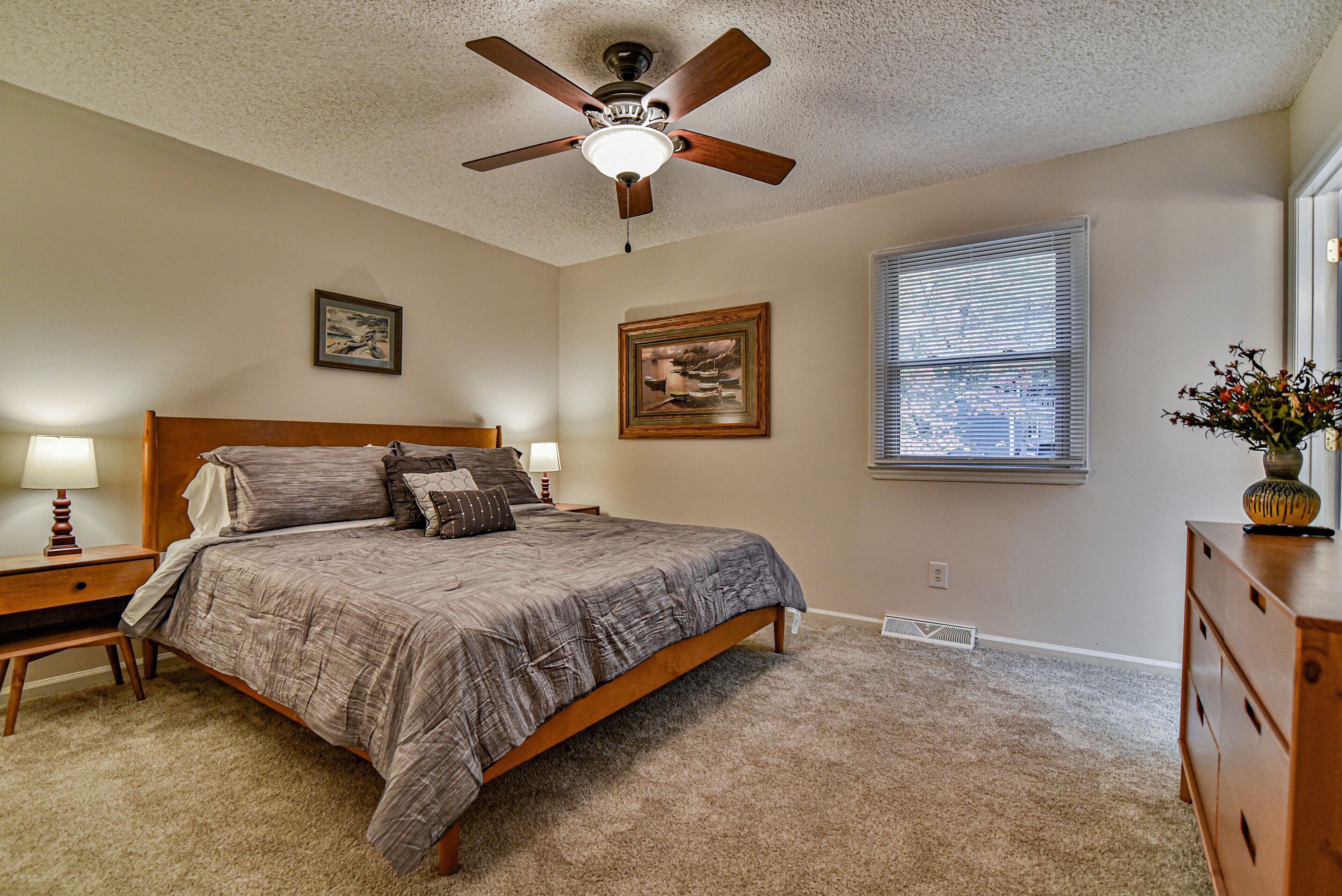 A bedroom with a bed, a ceiling fan, a nightstand, a dresser, and two wall-mounted pictures.