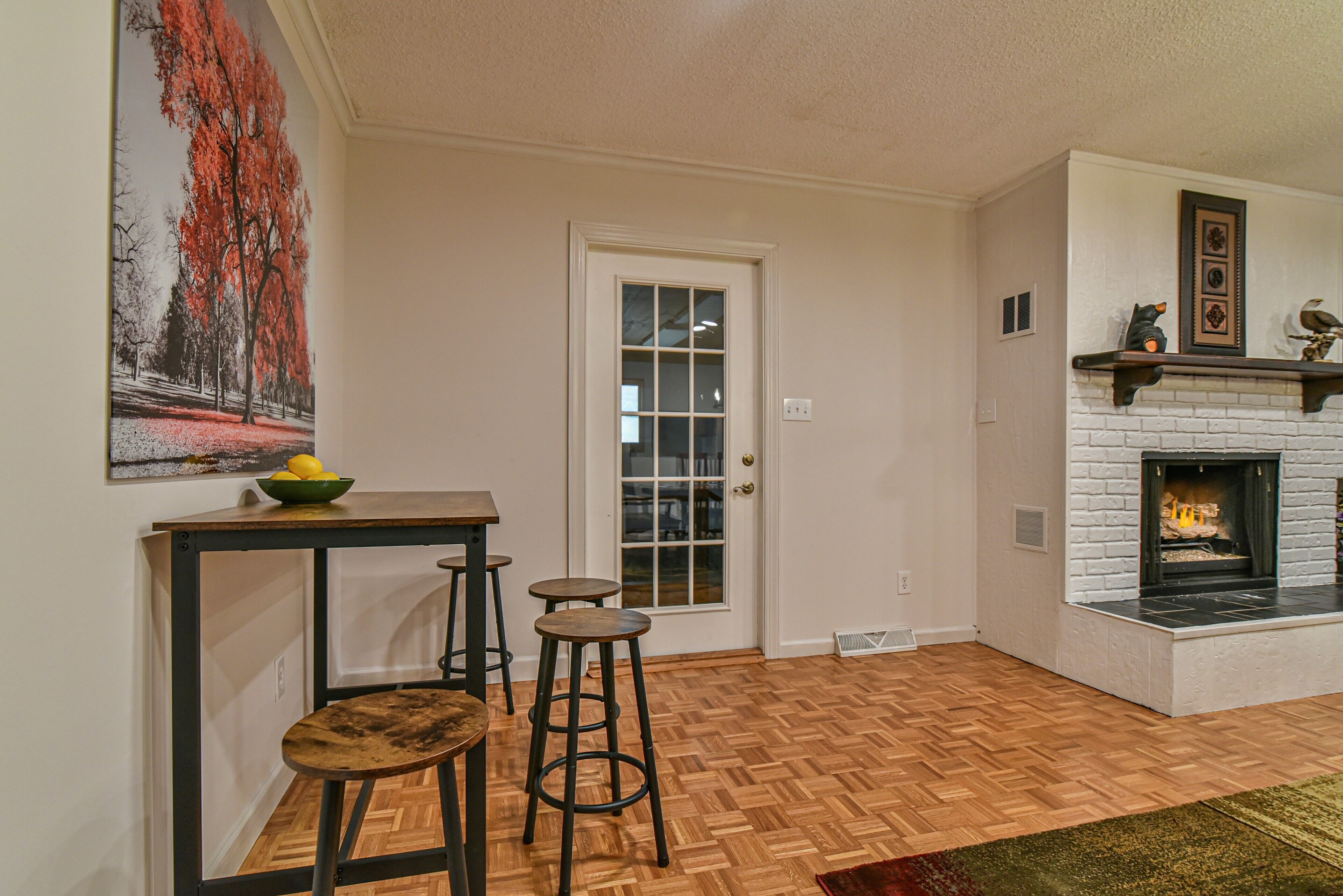 A room with a herringbone wood floor, a white fireplace, and a door with glass panels.