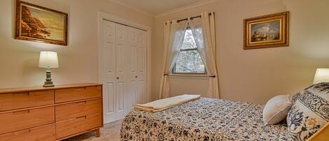 A bedroom with a bed, a dresser, a window with curtains, and two framed pictures on the wall.