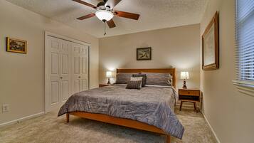 A bedroom with a bed, a ceiling fan, two bedside tables with lamps, and a door.