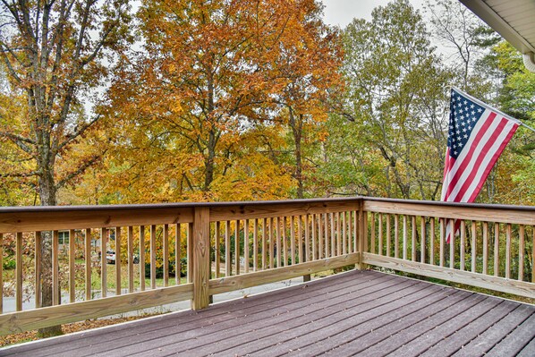 Une terrasse en bois avec une rambarde, un drapeau américain et, en arrière-plan, des arbres aux couleurs automnales.