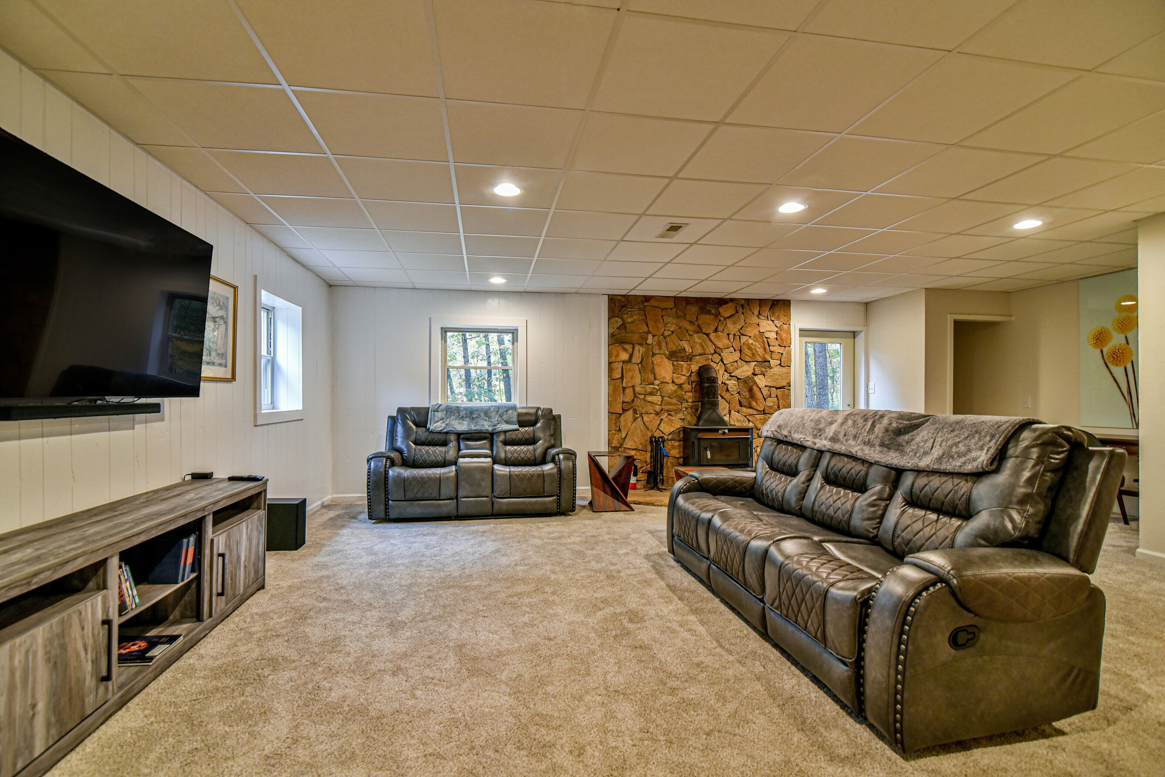 A living room with a stone wall, leather sofas, a flat-screen TV, and built-in shelves.