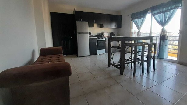 A spacious living area with a sofa, a dining table with chairs, a kitchen with modern appliances, and a balcony with curtains. - Departamentos Velasco,a 10 min del Centro,ideal Para Conocer Tijuana (Tijuana)