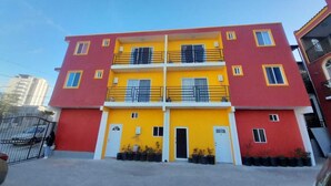 A multi-story building with a red and yellow facade, balconies, and a gated entrance. - Departamentos Velasco,a 10 min del Centro,ideal Para Conocer Tijuana (Tijuana)