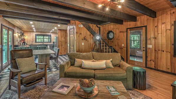 A cozy living room with a sofa, armchair, and coffee table. A staircase leads to a second floor.