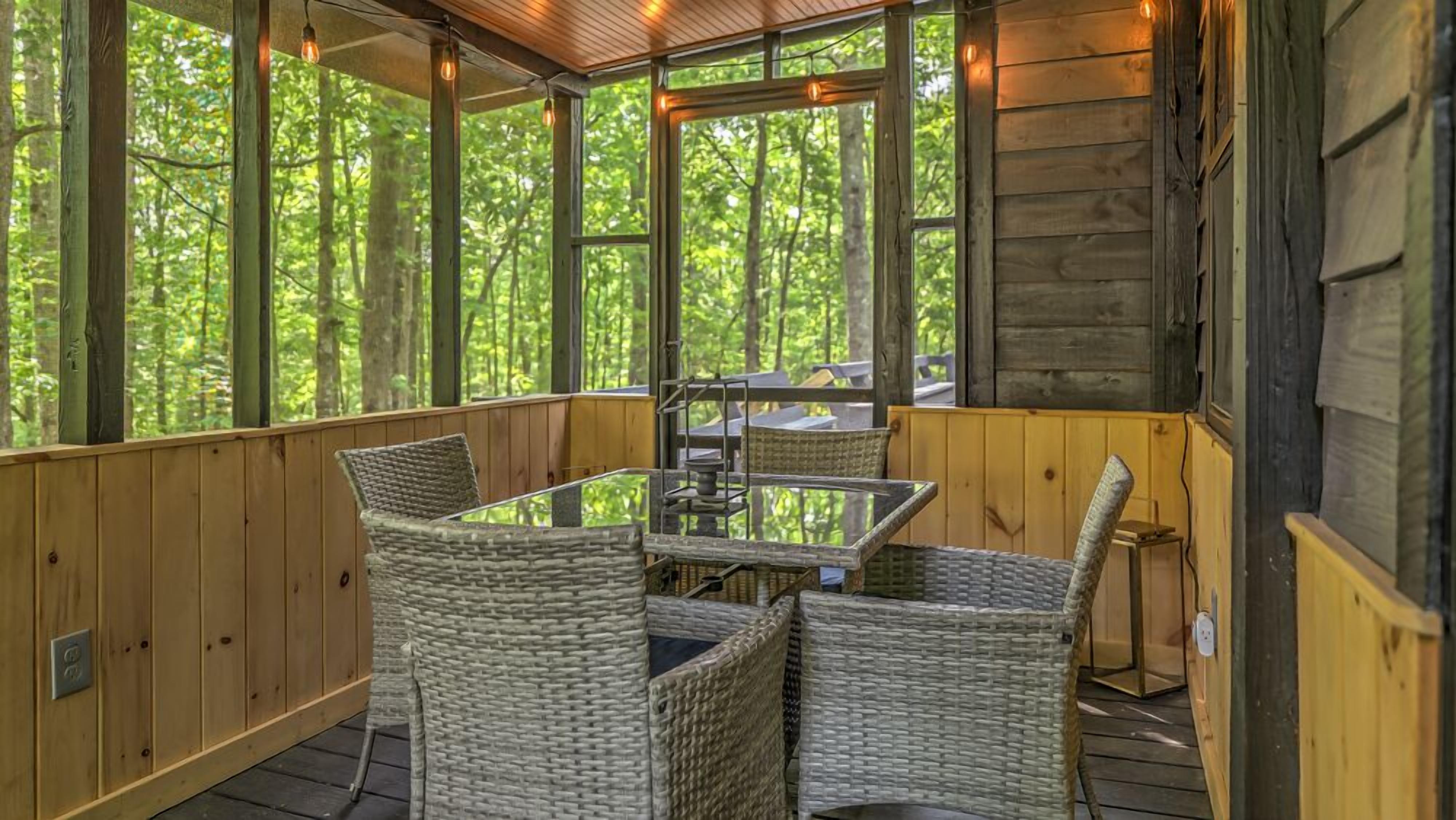 Un espace extérieur aménagé, abrité et doté de chaises en osier et d’une table en verre, entouré de murs en bois et de grandes fenêtres.