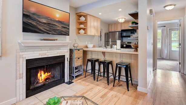 A modern kitchen with a fireplace, bar stools, and a large TV mounted above it.