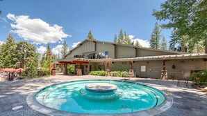 A pool area with a hot tub, surrounded by a brick patio, and a building with a covered deck and outdoor seating.