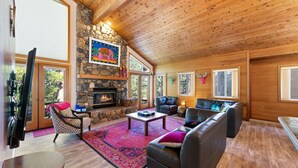 A cozy living room with a stone fireplace, leather sofas, and a large window overlooking the outdoors.