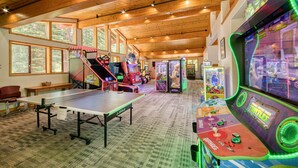 A spacious indoor area with a ping pong table, arcade games, and a large window overlooking a forest.