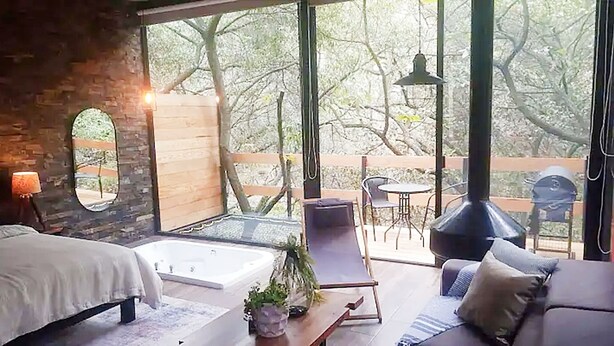 A modern bedroom with a large window, a bed, a seating area with a sofa, and a small table with a plant. - Loft Tree House 1 by Kivoya (Zapopan)